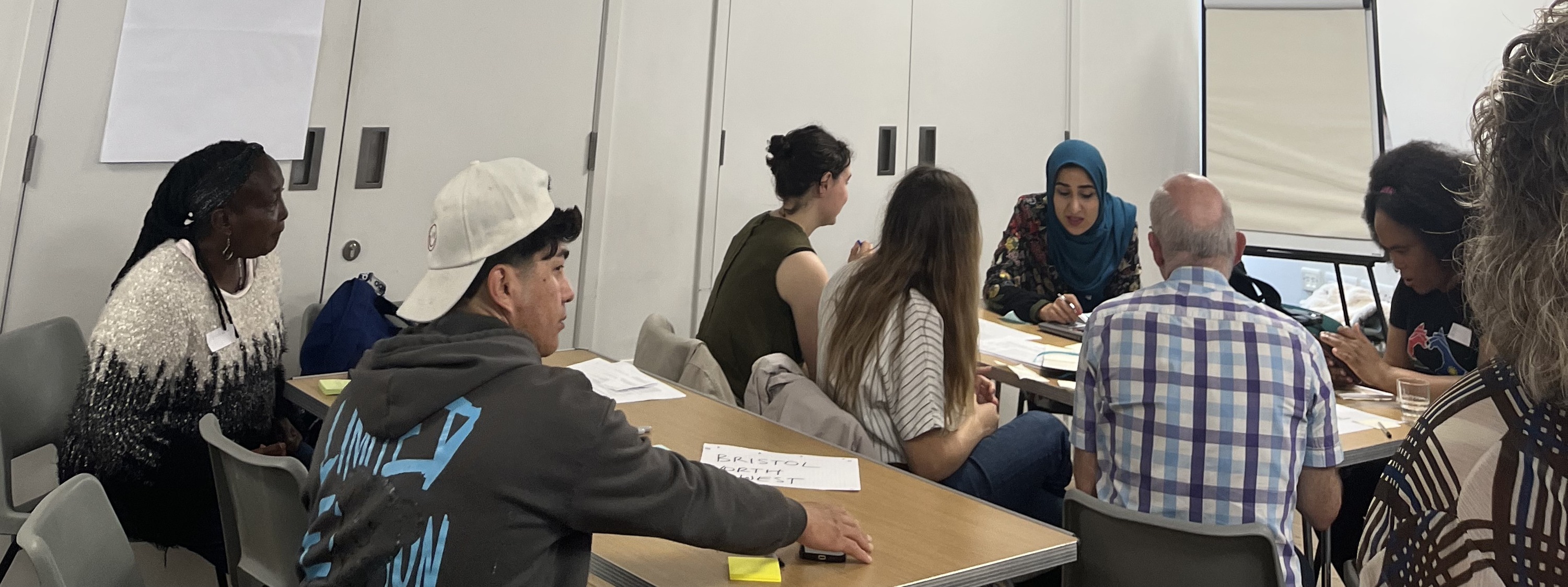 A group of people from mixed demographics sitting at tables listening to a facilitator