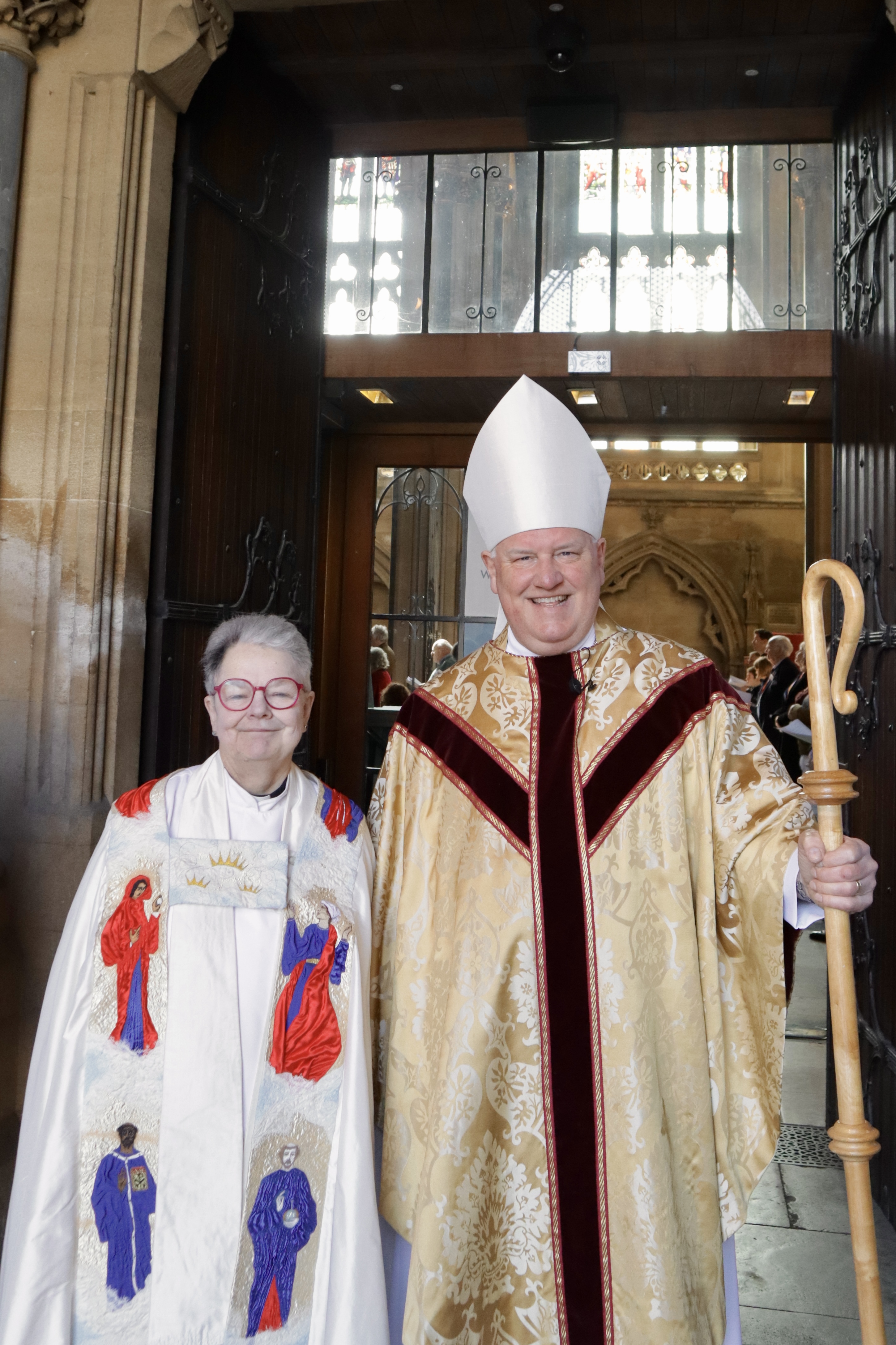 From left to right: Dean Mandy and Bishop Neil in their vestments, standing in the doorway of Bristol Cathedral