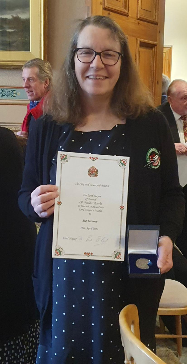 Photo of Sue Farrance holding her medal and certificate