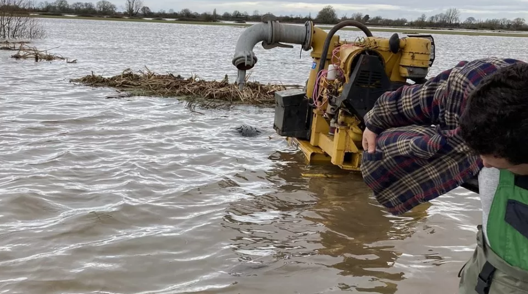 Image of farm flooded with water with big machinery pumping water out.