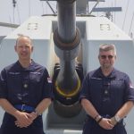 Two men stand in front of a Royal Navy gun