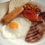 Plate of food containing fried egg, sausage, bacon, tomato, baked beans and toast